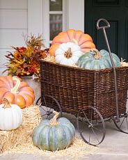 Assorted artificial pumpkins on top of hay bales and woven cart.