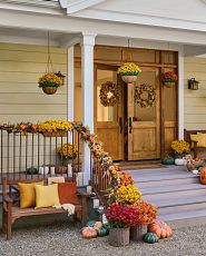Front porch decorated with artificial fall greenery and wooden bench with pillows and throw blanket