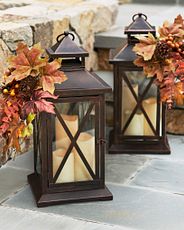 A pair of brown lanterns with artificial fall leaves and three candles