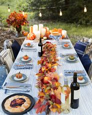 Outdoor dining table decorated with candles, pumpkins, blue and white plates, and an artificial fall garland as a centerpiece