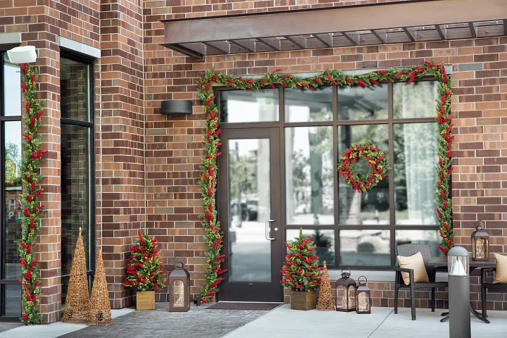 Brick wall exterior decorated with Christmas garlands, wreath, lanterns, and décor accents