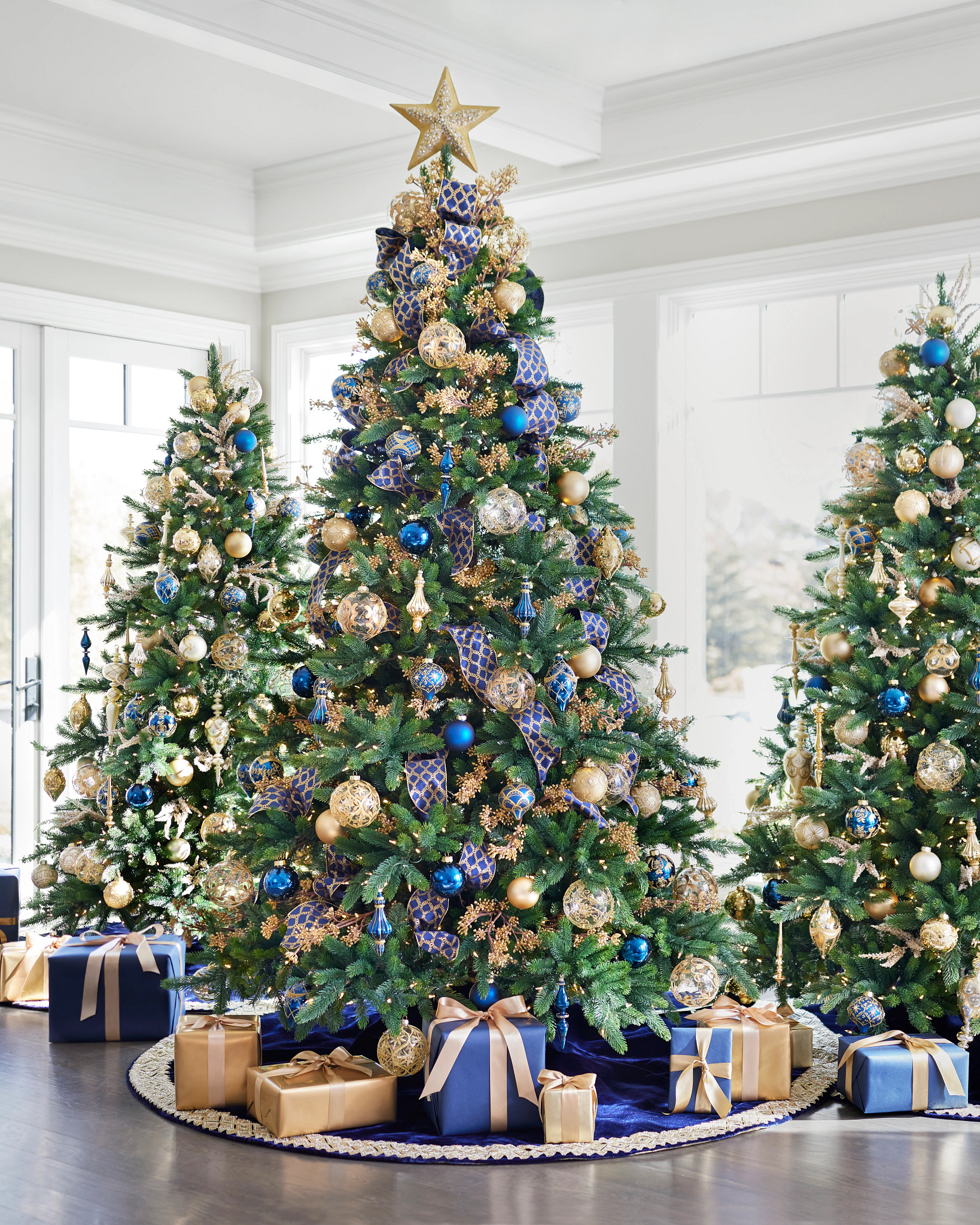Artificial Christmas trees decorated with sapphire and gold ornaments, ribbons, picks, tree topper, and tree skirt