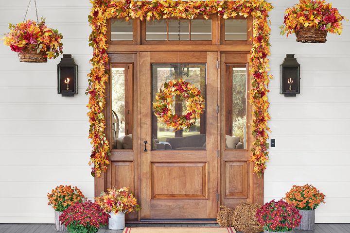 Front door with wreath, garland, and potted foliage in fall colors