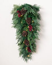Pre-lit artificial Christmas swag with faux cedar, fir, berries, and pinecones on white wall