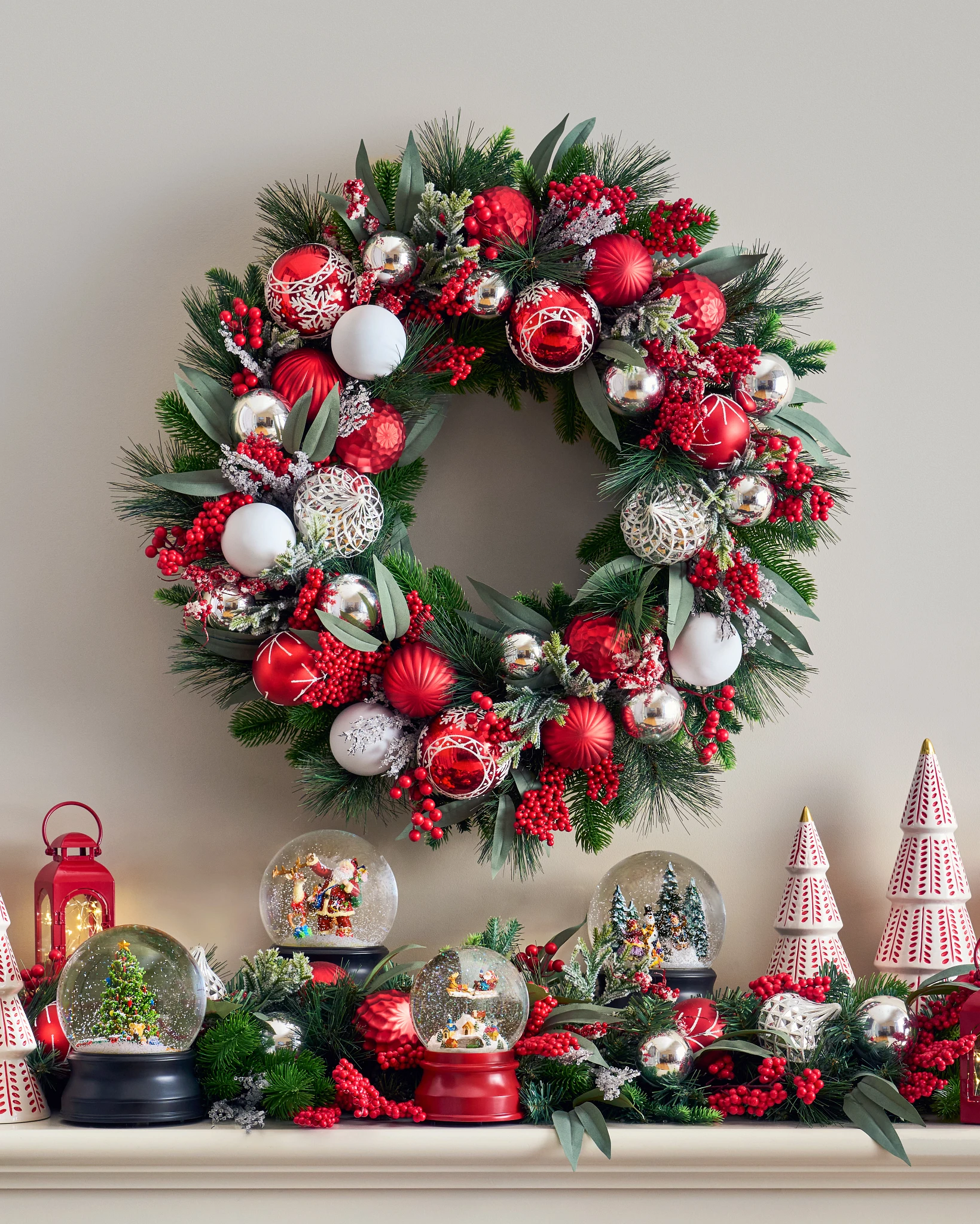 Selection of snow globes on a white mantel with a red and silver Christmas wreath