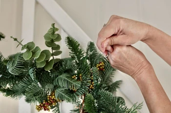 Woman securing foliage of artificial Christmas garland to staircase handrails with clear string