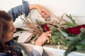Woman decorating artificial garland with branch and flower picks