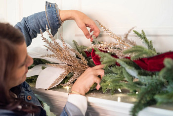 A woman decorating a garland with white magnolia branch picks, metallic beaded branch picks, and red velvet ribbon