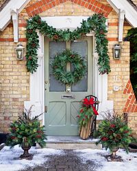 Front porch decorated with wreath, garland, Christmas sled, and potted foliage