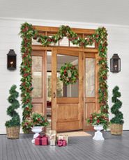 Light brown front door decorated with artificial Christmas greenery and topiaries