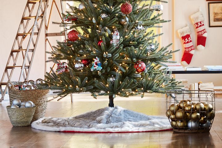 Artificial Christmas tree with tree skirt next to baskets of gold and silver ornaments