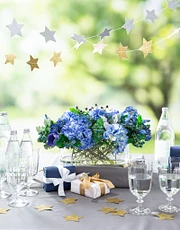 Blue floral centerpiece on a table with drinking glasses, a star garland, and wrapped presents