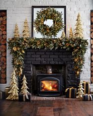 A fireplace decorated with Christmas wreaths, garlands, and accent trees