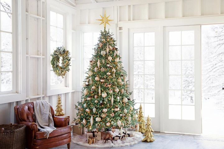 Artificial Christmas tree by wide windows decorated with gold ornaments.
