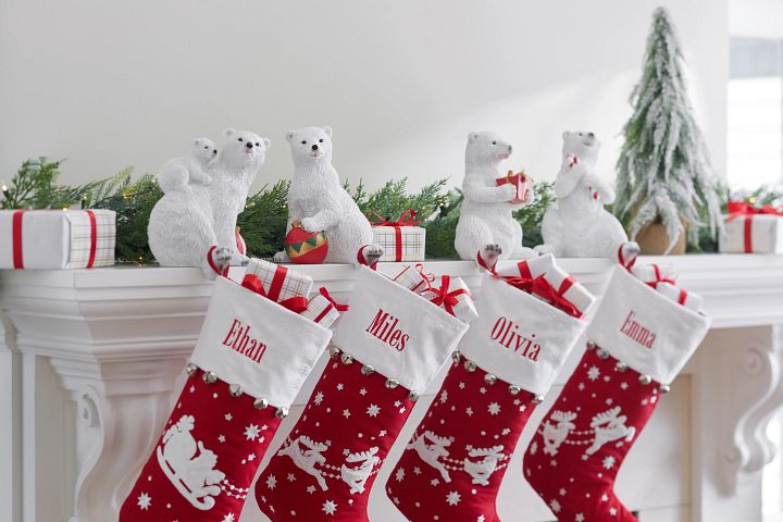 White fireplace mantel decorated with red and white Christmas stockings, polar bear stocking holders, and artificial foliage