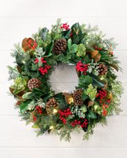 Artificial Christmas wreath decorated with lights, faux berries, pinecones, and magnolia leaves