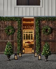 Outdoor barn doors decorated with artificial wreaths, garlands, potted topiaries, lights, and lanterns