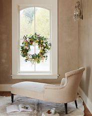 Ivory chaise lounge facing a window decorated with artificial flower wreath