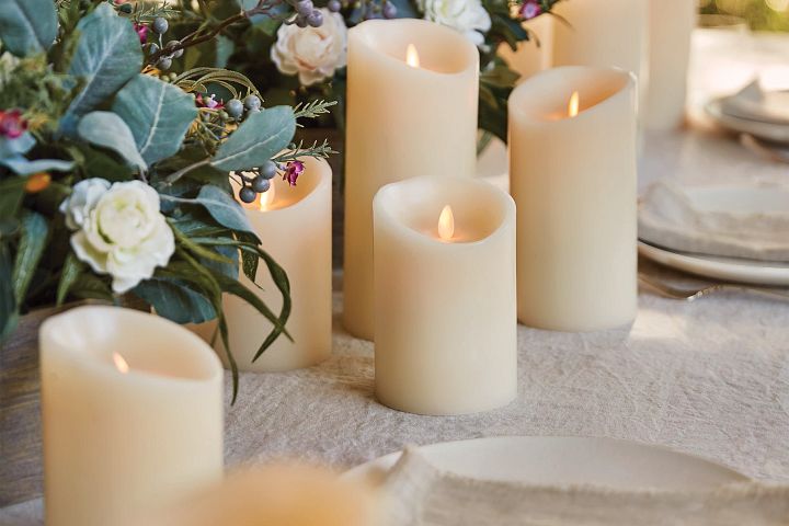 Flameless LED pillar candles in assorted heights with artificial flowers and place settings displayed on beige table cloth