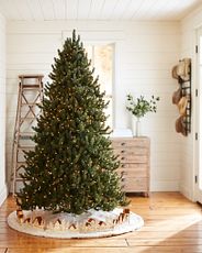 Pre-lit artificial Christmas tree displayed with ivory faux fur skirt and decorative Christmas village collar