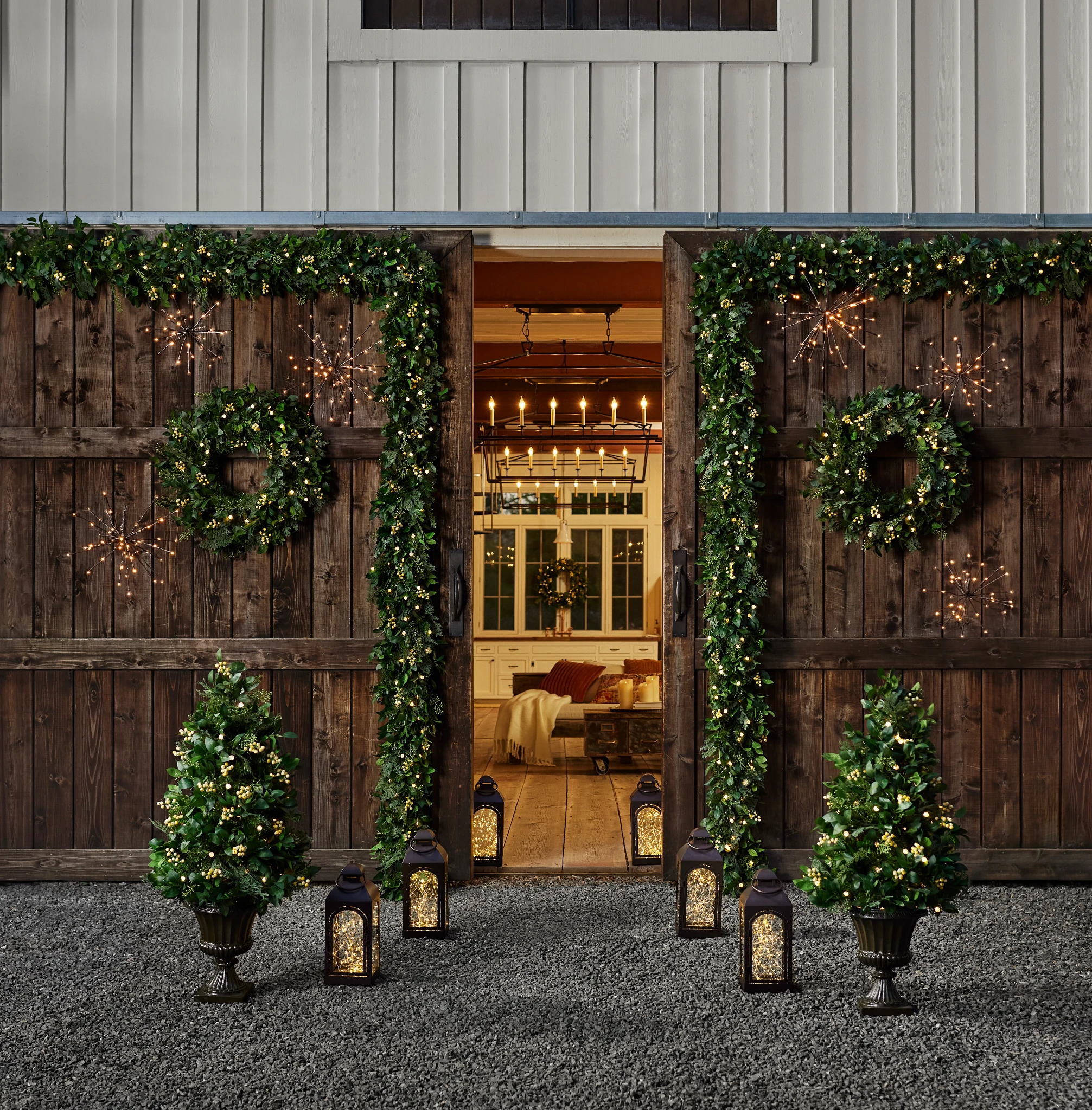 Outdoor barn doors decorated with artificial Christmas greenery, lights, and lanterns