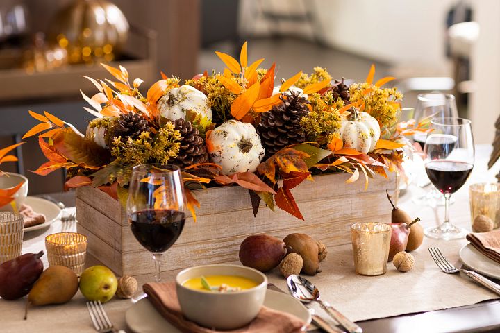 A fall centerpiece with pumpkins and pinecones displayed on the dining table