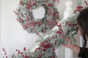 Woman fluffing foliage of artificial frosted Christmas garland on stair banister