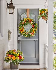 Gray front door with artificial wreath with orange and yellow flowers