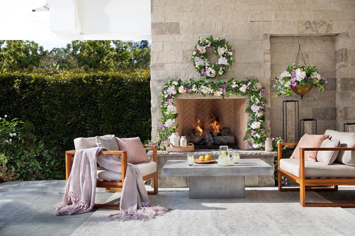 Outdoor seating area and fireplace decorated with artificial flower wreath, garland, and hanging basket