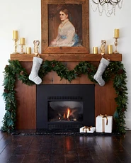 Wooden fireplace mantel decorated with a painting, evergreen garland, and Christmas stockings