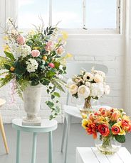 Assorted artificial flower arrangements set on stools against white brick wall and window