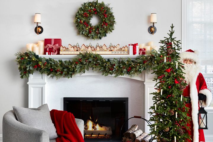  White mantel decorated with artificial greenery, Christmas village advent calendar, and candles
