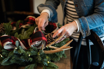 Hands decorating a Christmas wreath with antler picks and pinecones