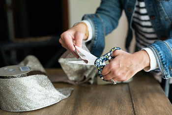 Hands cutting the ends of a scalloped Christmas tree ribbon with scissors