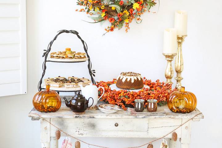 Side table food spread decorated with fall wreaths, candles, and glass pumpkins