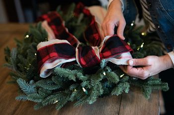 Hands adding ribbon bow to artificial Christmas wreath