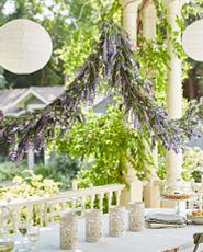 Outdoor dining area decorated with artificial lavender garland, white round paper lanterns, and white candle hurricanes