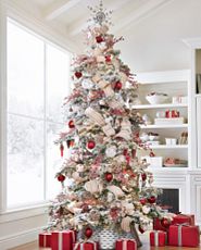 Artificial frosted Christmas tree decorated with woodland-inspired ornaments, red and white ornaments, and red berry picks