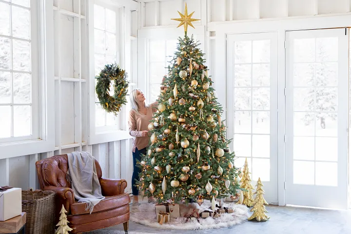 Woman decorating Christmas tree with tree topper, ornaments, lights, and more