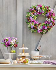 Dessert table spread decorated with pink and purple artificial flower arrangement and wreath