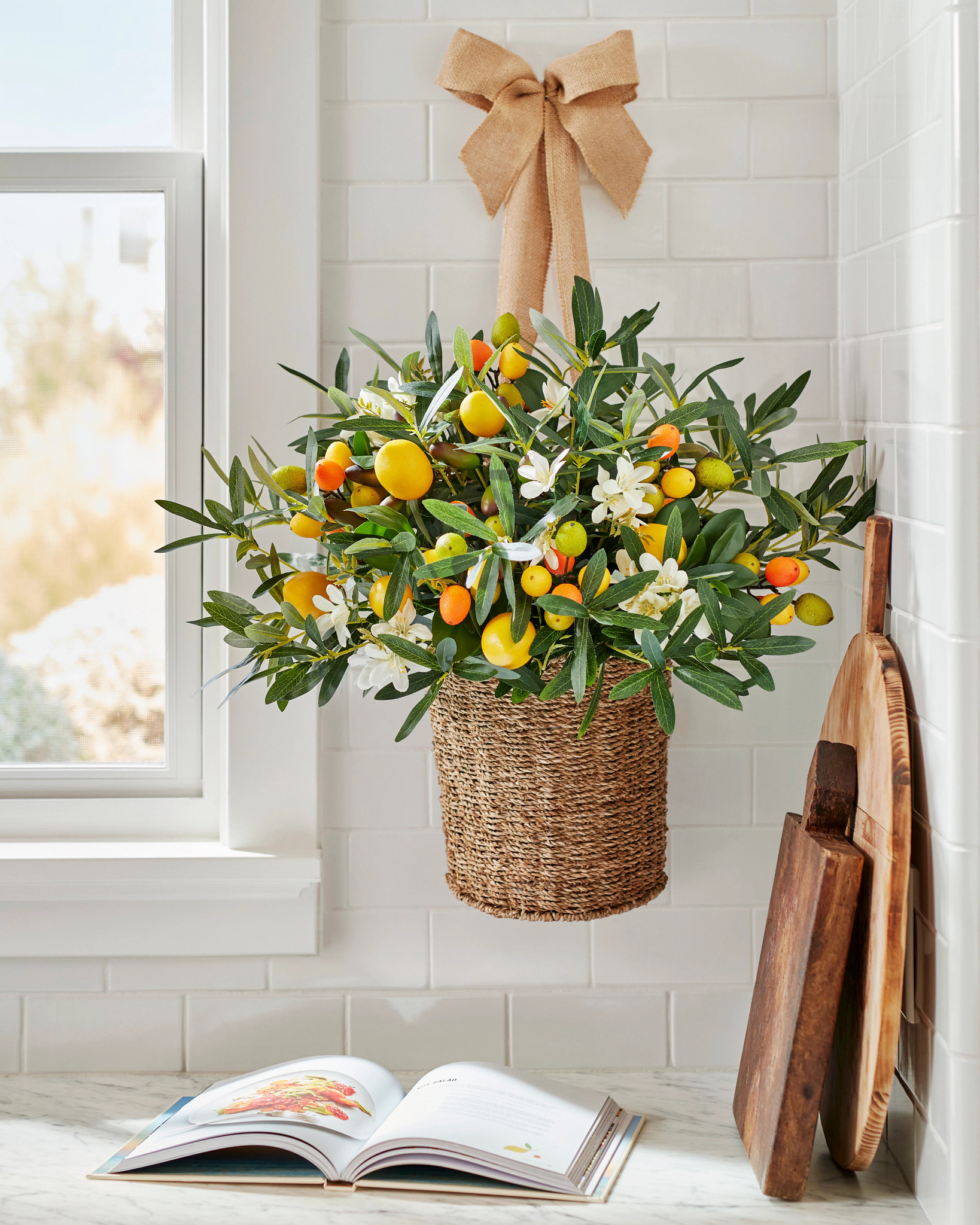 Orange and yellow blooms in a hanging basket, a cookbook, and wooden chopping boards in corner