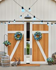 Double barn doors decorated with blue festoon lights, wired rabbit sculptures, and artificial spring foliage featuring daisies, forget-me-nots, lisianthus, baby's breath, and ivy leaves