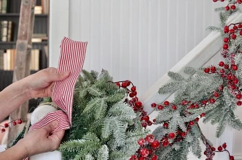 Hands looping red pinstriped ribbon through an artificial Christmas wreath
