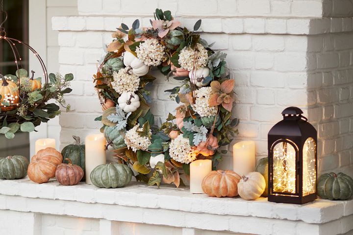 Fireplace mantel decorated with fall foliage, pumpkins, candles, and lanterns