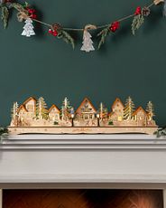 A wooden Christmas village lit with amber LED lights displayed on a mantel