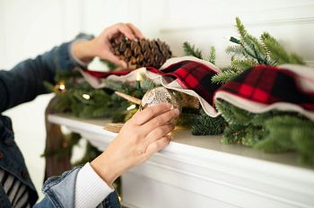 Zwei Hände beim Dekorieren mit einer künstlichen Weihnachtsgirlande