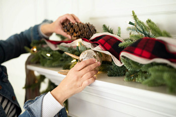 Hands decorating a Christmas garland with pinecones and gold Christmas ornaments