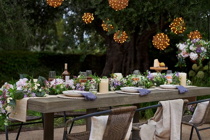 Outdoor dining table decorated with artificial spring garland, candles, wine glasses, and place settings