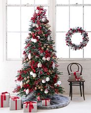 Artificial Christmas tree decorated with red and white ornaments, berry picks, and gray faux fur tree skirt