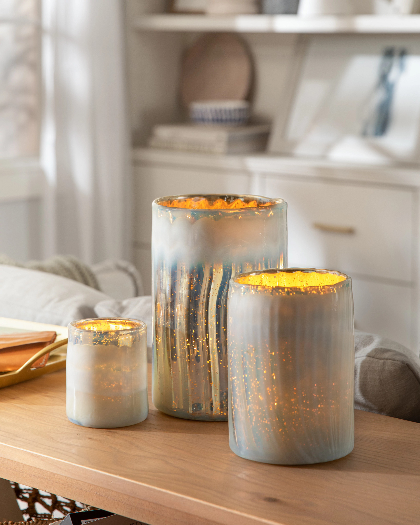 Set of three mercury glass hurricanes with a creamy white finish on top of a console table in the living room